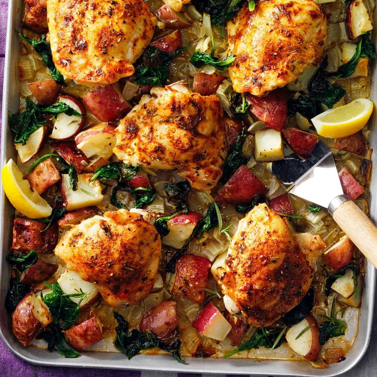 Sheet pan with roasted chicken, vegetables, and lemon wedges on a purple surface